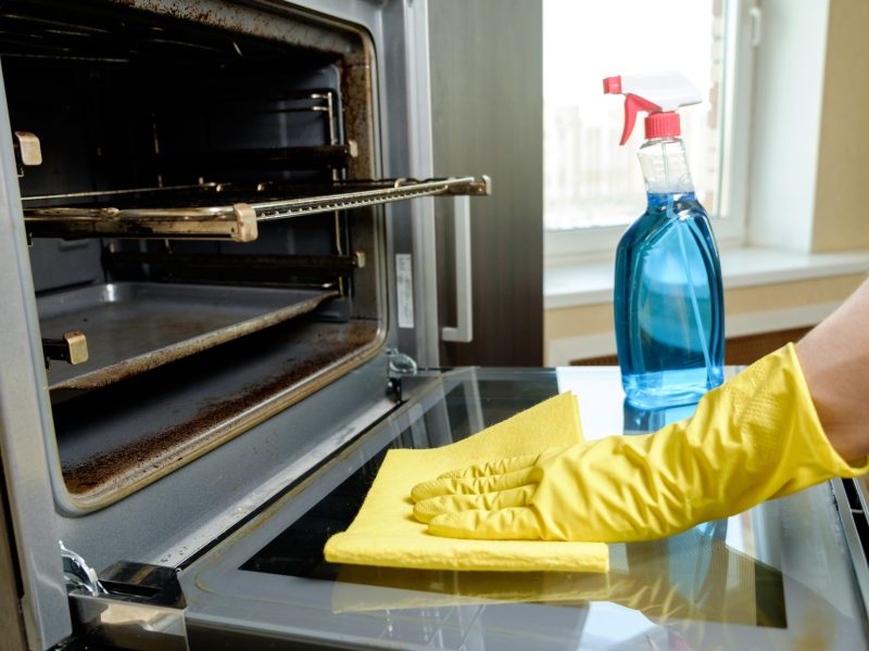 Man with bottle of spray and rag cleaning oven at home kitchen. Housework and housekeeping concept