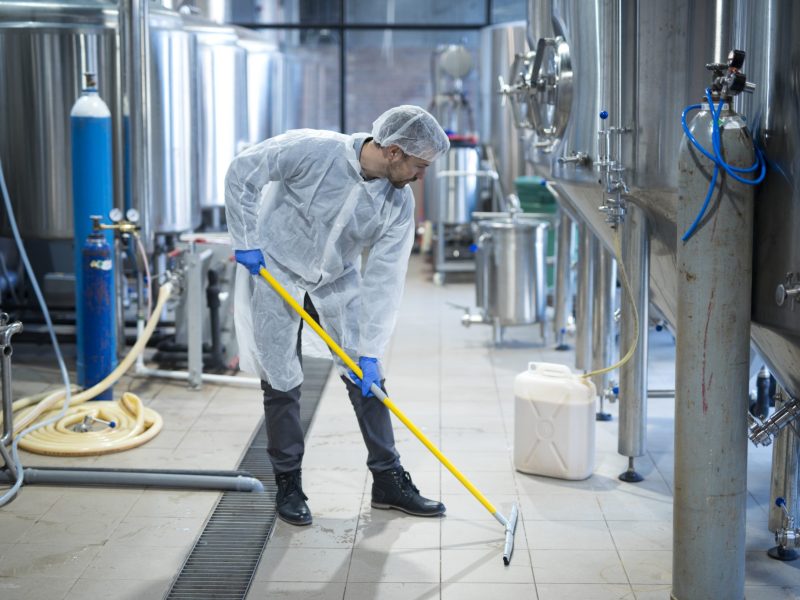 Professional industrial cleaner in protective uniform cleaning floor of food processing plant.