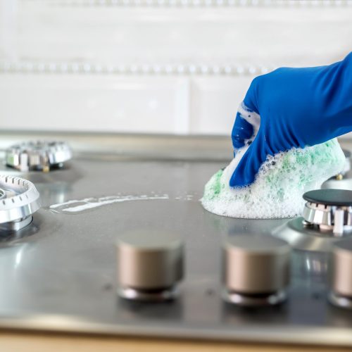 Woman with sponge and rubber protective glove used to wipe down an oven range top