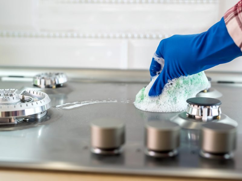 Woman with sponge and rubber protective glove used to wipe down an oven range top